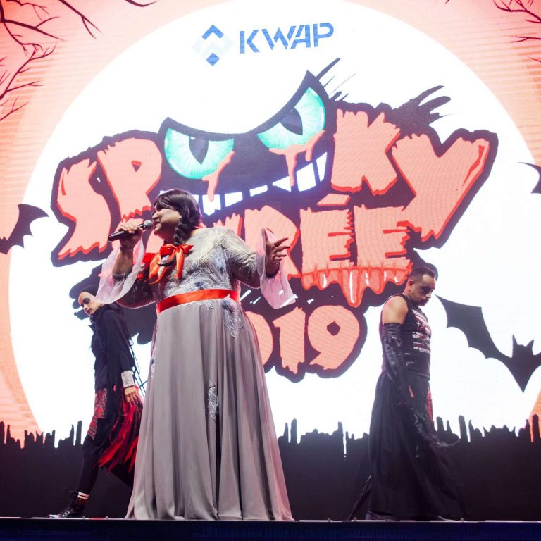 A woman dressed in white sings into a microphone on stage at the KWAP Spooky Soiree 2019 event in KLCC.